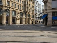 two buildings and people walking down the street next to the tram tracks is the corner of a large, busy city square
