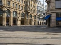 two buildings and people walking down the street next to the tram tracks is the corner of a large, busy city square