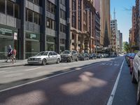 cars line the street on both sides of a busy city street with tall buildings and bicycles