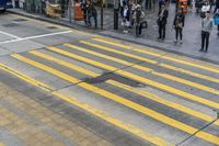 people are waiting to cross the street at an intersection on the corner of a busy sidewalk
