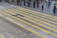 people are waiting to cross the street at an intersection on the corner of a busy sidewalk