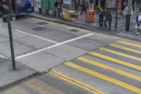 people are waiting to cross the street at an intersection on the corner of a busy sidewalk