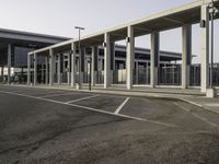 a parking lot next to an airport with many windows and pillars on both sides, two buildings