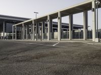 a parking lot next to an airport with many windows and pillars on both sides, two buildings