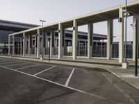 a parking lot next to an airport with many windows and pillars on both sides, two buildings