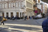 a busy sidewalk in the city with people walking along it on the road beside parked cars