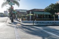 the corner of a busy street next to a restaurant and a parking meter, trees and the sidewalk