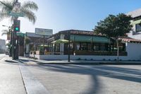 the corner of a busy street next to a restaurant and a parking meter, trees and the sidewalk