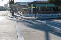 the corner of a busy street next to a restaurant and a parking meter, trees and the sidewalk