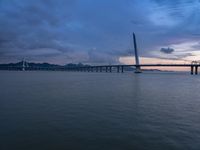 a large bridge spanning over a river under a blue sky during sunset or at night