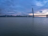 a large bridge spanning over a river under a blue sky during sunset or at night