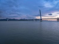 a large bridge spanning over a river under a blue sky during sunset or at night