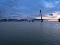 a large bridge spanning over a river under a blue sky during sunset or at night