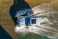 a white suv driving through water on a dirt road in the sun at dusk or afternoon