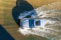 a white suv driving through water on a dirt road in the sun at dusk or afternoon