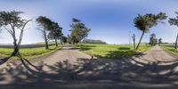 a three way street in a large field and grassy area with trees lining the roadway