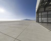 an airplane is parked outside a hangar with mountains in the background and sun shining in the sky