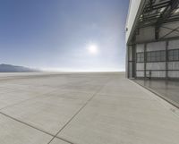 an airplane is parked outside a hangar with mountains in the background and sun shining in the sky