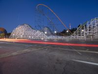 a roller coaster and other rides sitting on the road near an amusement park at dusk