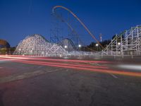 a roller coaster and other rides sitting on the road near an amusement park at dusk