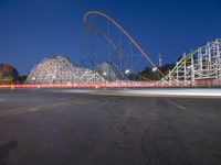 a roller coaster and other rides sitting on the road near an amusement park at dusk