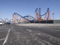 a view of a roller coaster from the back side of a road with parked cars