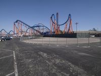 a view of a roller coaster from the back side of a road with parked cars