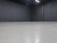 a empty room with concrete floor in it, on the corner is a bright white light