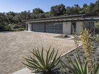 an empty garage surrounded by plants and trees in front of a house that has been designed to look modern