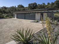 an empty garage surrounded by plants and trees in front of a house that has been designed to look modern