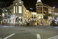 a city at night with a clock tower and shops lined up and illuminated, across from each other