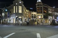 a city at night with a clock tower and shops lined up and illuminated, across from each other