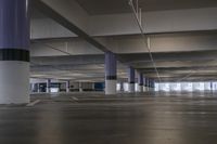 a parking garage has long columns near some large windows, concrete floors and yellow lights