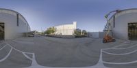 a wide angle photo of a building and crane in a parking lot with other structures