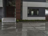 a white fence on the sidewalk in front of a house in the rain and some green bushes