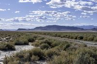 a vast, arid landscape with clouds in the blue sky above a mountain range and open field