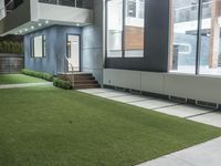 a backyard with artificial turf is illuminated by recessed lighting and outdoor lighting on the side of the house