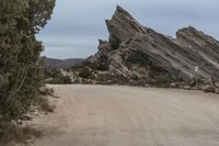 a paved desert dirt road with a sign warning of dangerous driving past boulders in the background