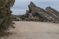 a paved desert dirt road with a sign warning of dangerous driving past boulders in the background