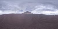 a barren hillside with hills covered in brown colored sand, surrounded by dark clouds and mountains