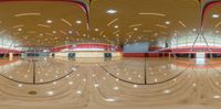 a wide angle view of an empty basketball court and hard wood floors with lights shining in the ceiling