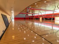 a gym with red and black walls and hardwood floors with a basketball hoop attached to the ceiling