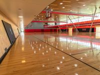 a gym with red and black walls and hardwood floors with a basketball hoop attached to the ceiling