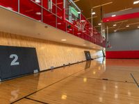 a gym with a wooden floor and red lighting fixtures on the wall and flooring