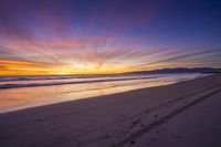 sunset sky with waves rolling on the beach in front of the ocean and mountains in the distance