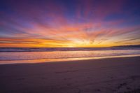 sunset sky with waves rolling on the beach in front of the ocean and mountains in the distance