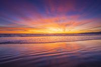 sunset sky with waves rolling on the beach in front of the ocean and mountains in the distance