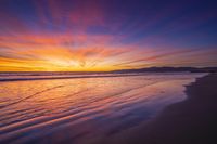 sunset sky with waves rolling on the beach in front of the ocean and mountains in the distance