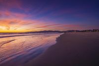 sunset sky with waves rolling on the beach in front of the ocean and mountains in the distance