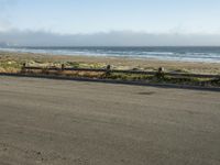 an empty beach road lined with wooden posts and fenced in bench on one side